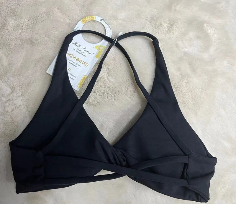 KiKis black padded front twist sports bra with adjustable straps laid on beige surface