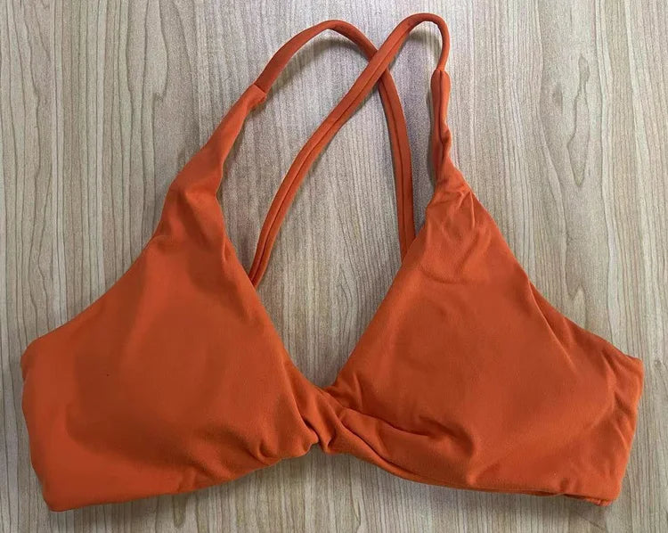 Orange padded front twist sports bra with thin double straps laid flat on wooden surface