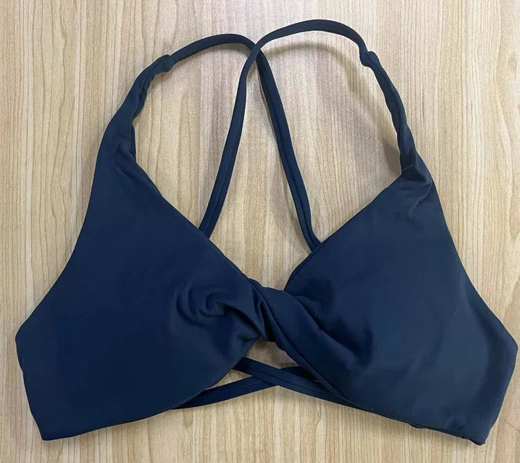KiKis black padded front twist sports bra with crisscross straps on wooden background