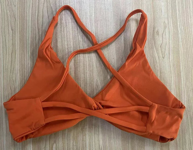 Orange padded front twist sports bra with cross-back straps by KiKis laid flat on wooden surface