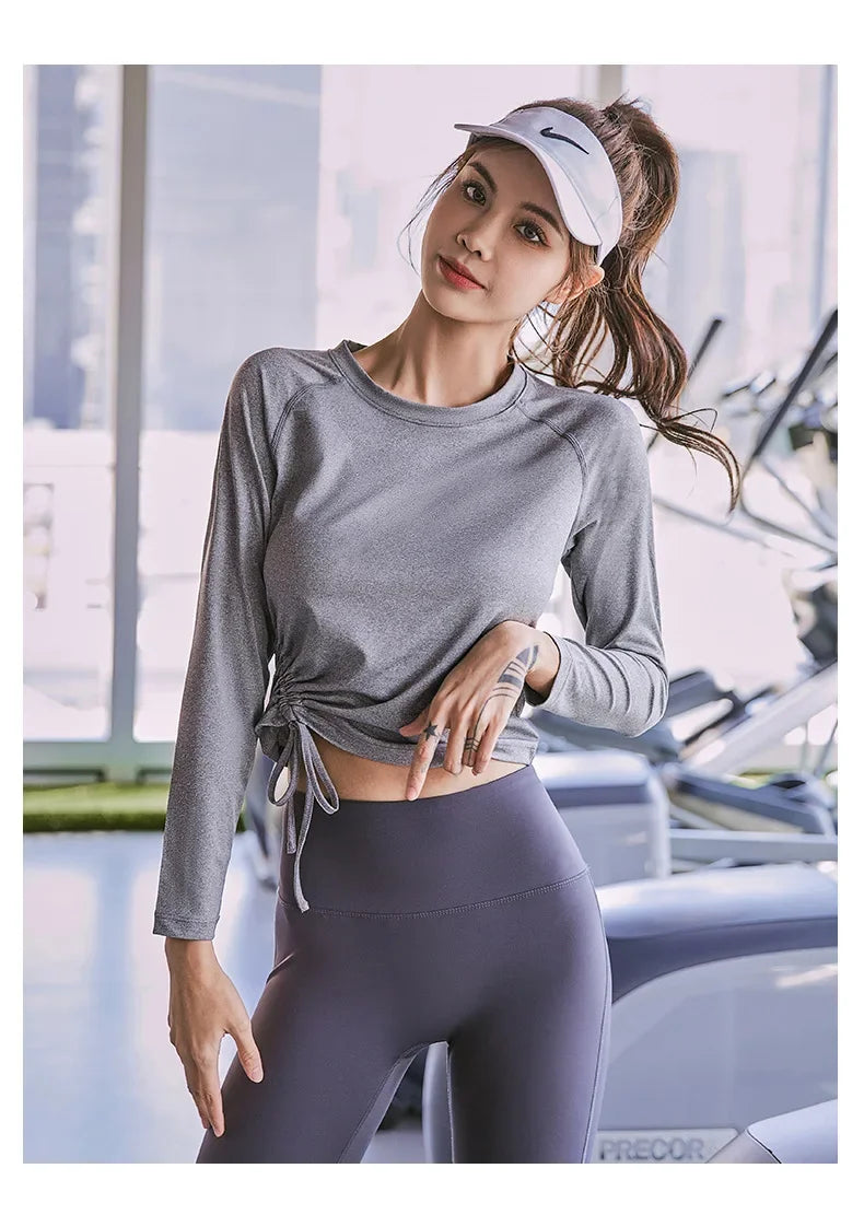 KiKis women's long sleeve yoga top in gray with side tie detail, worn by woman in gym setting