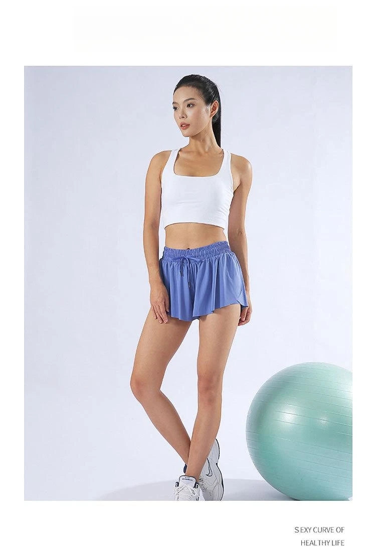 Woman wearing blue KiKis yoga running skirt shorts for women paired with white sports bra and sneakers