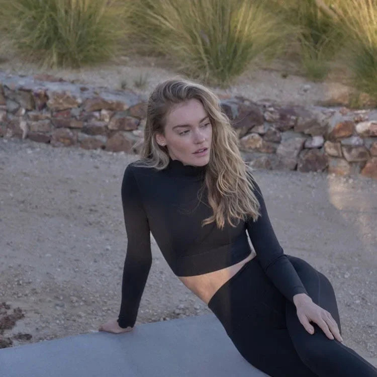 Woman wearing a black long sleeve lace back yoga top from KiKis while sitting outdoors on concrete