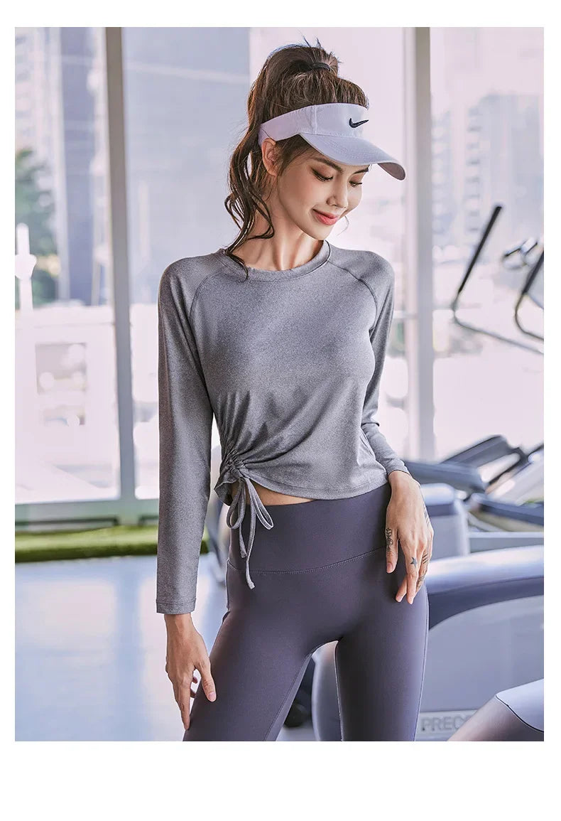 KiKis women's long sleeve yoga top in gray with side tie detail worn during indoor workout