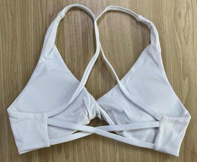 KiKis white padded front twist sports bra with adjustable straps laid flat on wooden surface