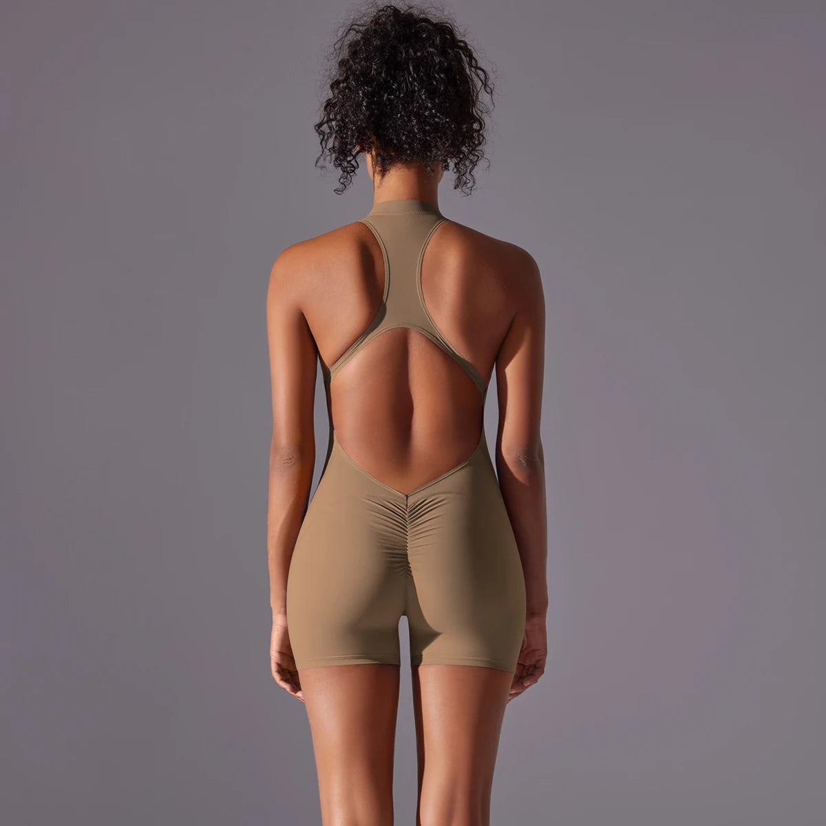 Back view of woman wearing a khaki backless gym bodysuit for women with racerback design and shorts
