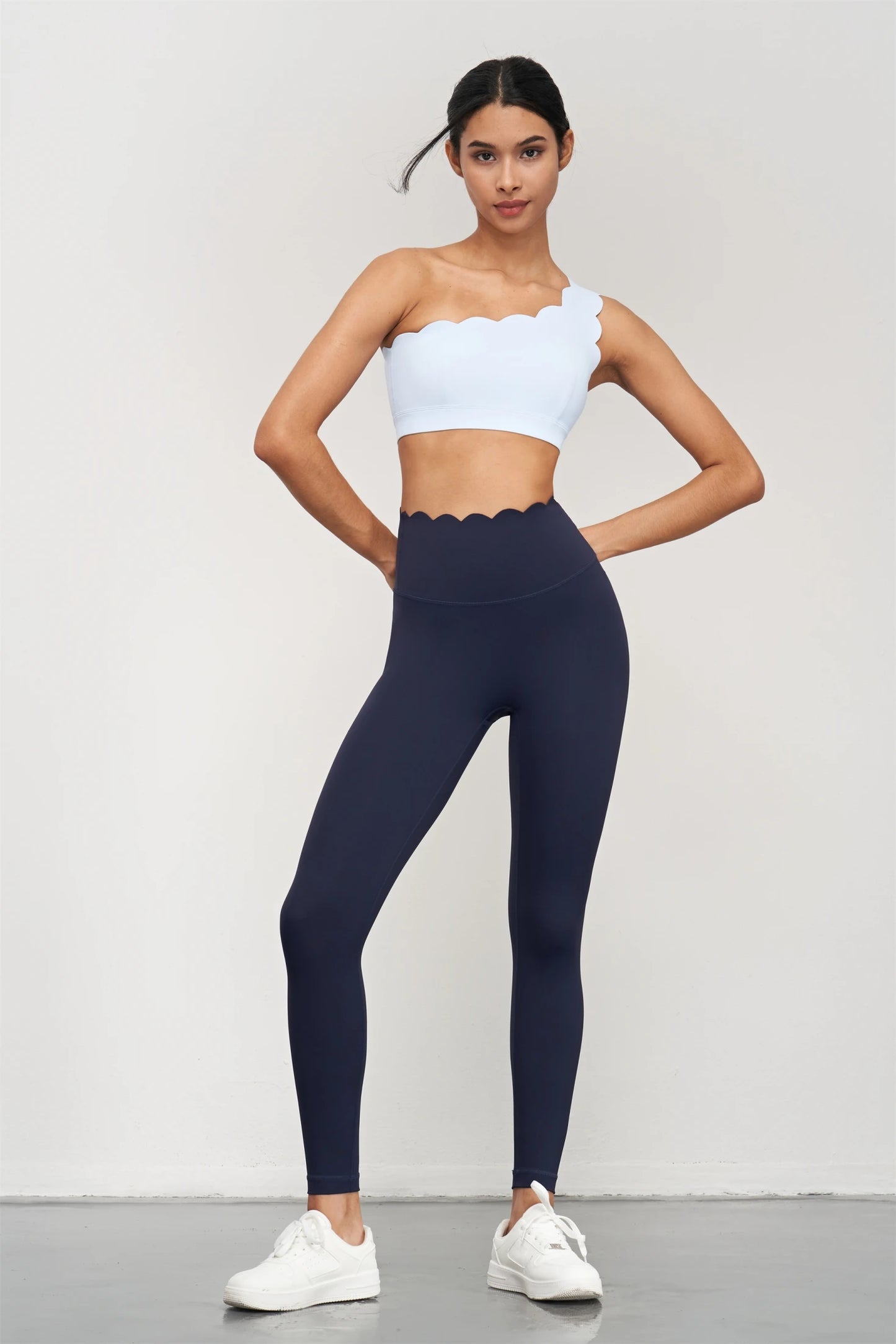 Woman wearing KiKis Women Seamless Lotus Arc Yoga Pants in black with scalloped waist and white crop top