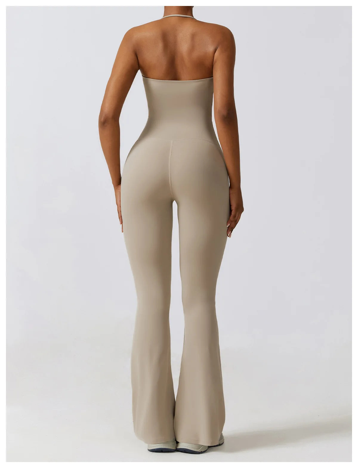 Back view of a woman wearing a beige one piece yoga suit for women with a strapless design