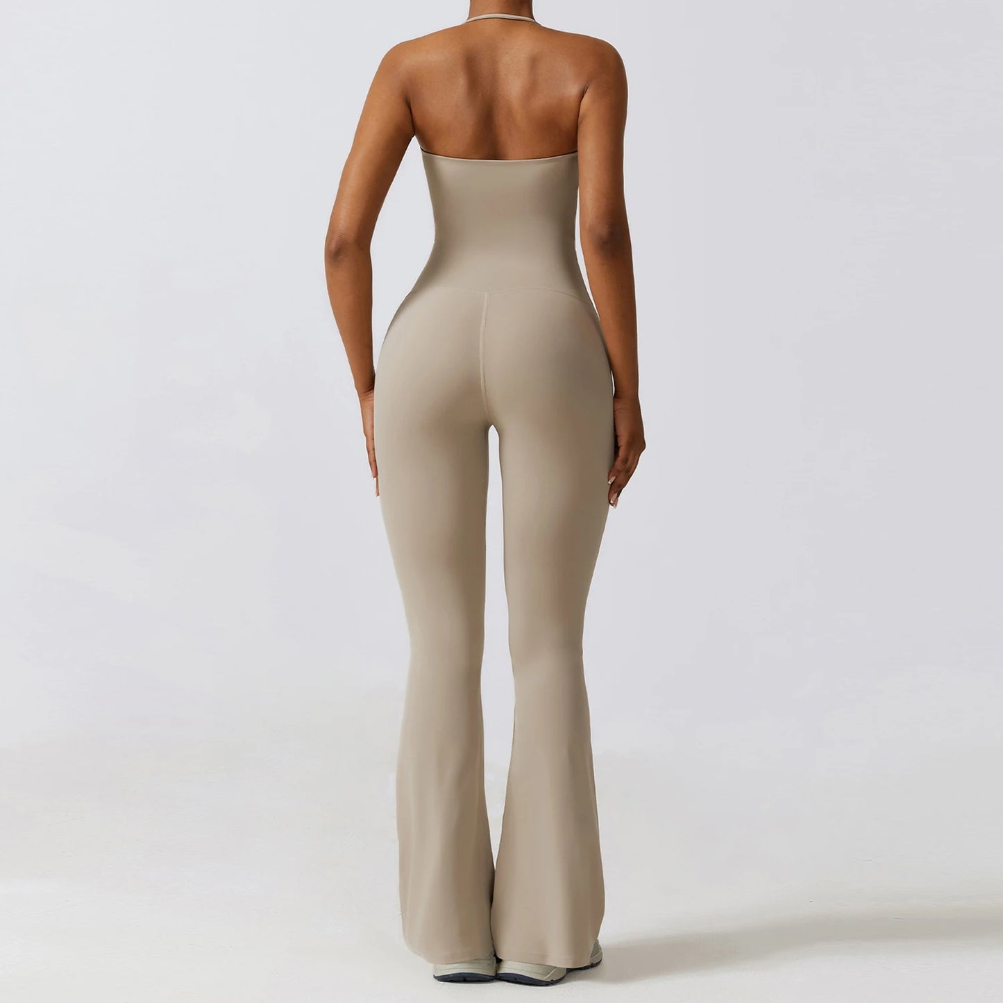 Back view of a woman wearing a beige one piece yoga suit for women with flared legs