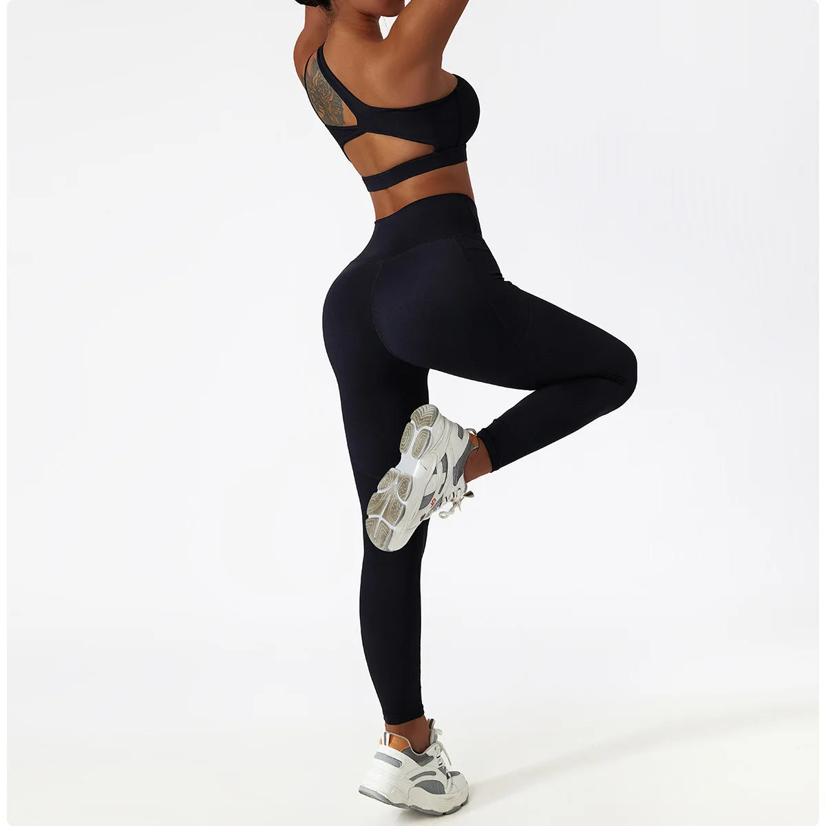 Black one shoulder sports bra and leggings set by KiKis worn by a woman in active pose