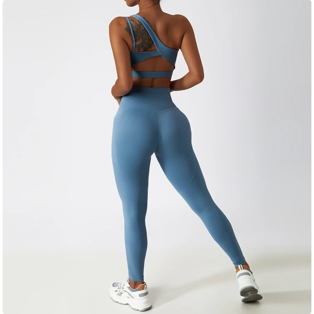Woman wearing KiKis one shoulder sports bra and leggings set in blue with lace detail and white sneakers