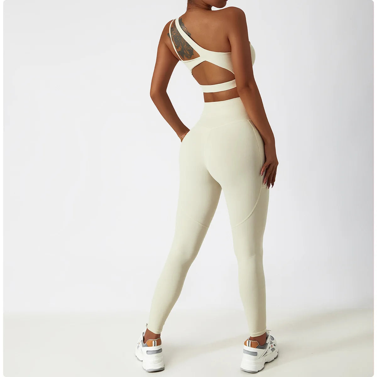 KiKis cream one shoulder sports bra and leggings set worn by woman with tattoo and white sneakers