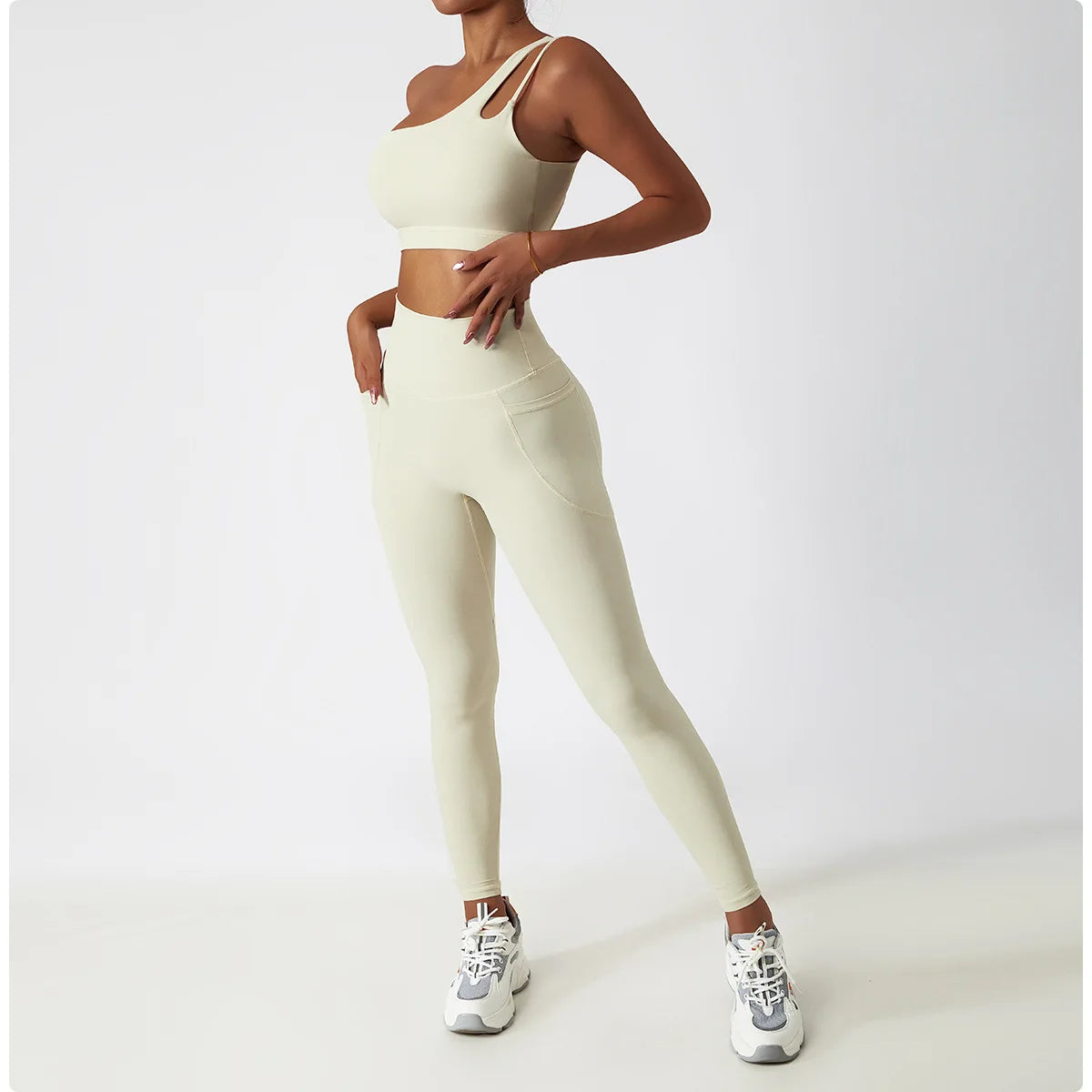 Cream one shoulder sports bra and leggings set by KiKis modeled with white sneakers