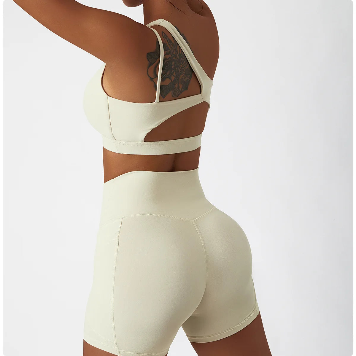 Woman wearing beige one shoulder sports bra and leggings set showing back and side details