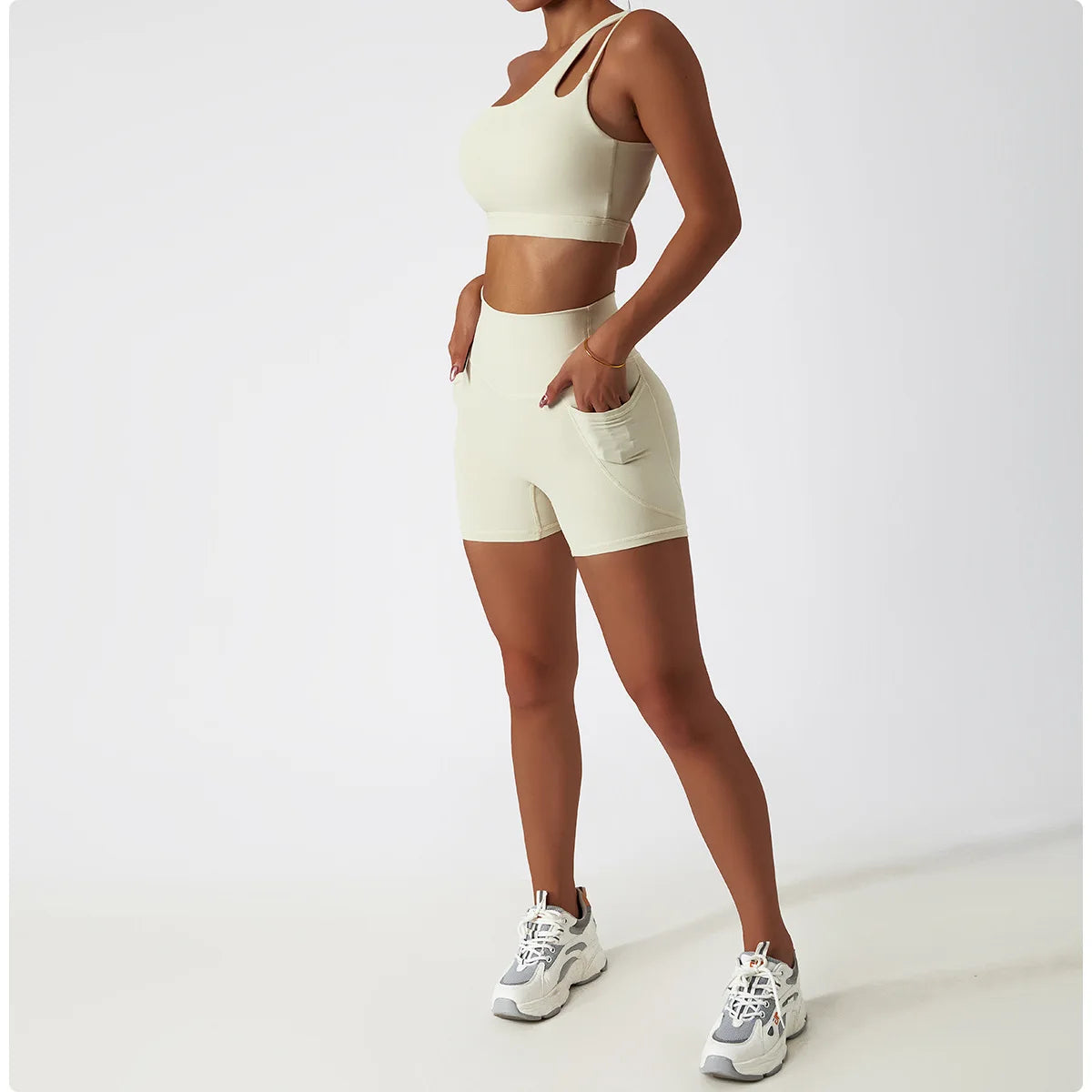 KiKis beige one shoulder sports bra and leggings set with shorts worn by model with white sneakers