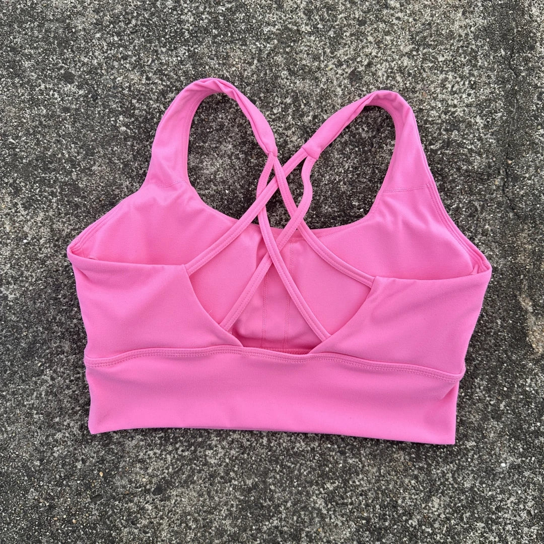 Pink cross back sports bra for women laid flat showing crisscross straps and seamless design