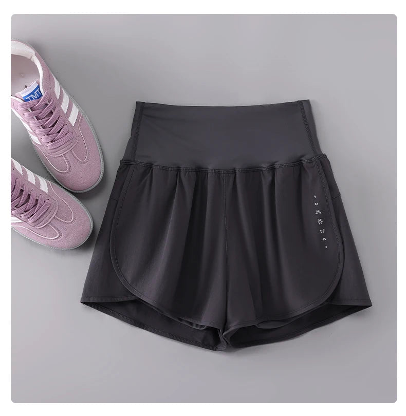 KiKis black Womens Running Shorts with high waist and side pocket detail next to pink sneakers