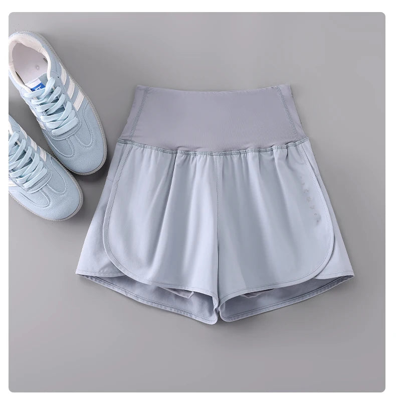 Light gray KiKis womens running shorts with high waistband displayed next to light blue sneakers
