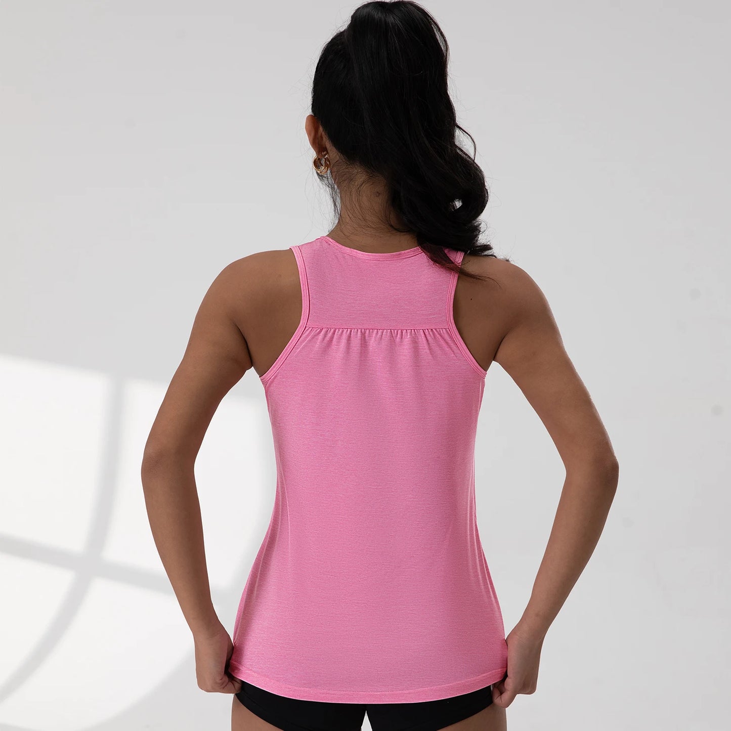 Back view of woman wearing pink round neck sleeveless gym top by KiKis with black shorts