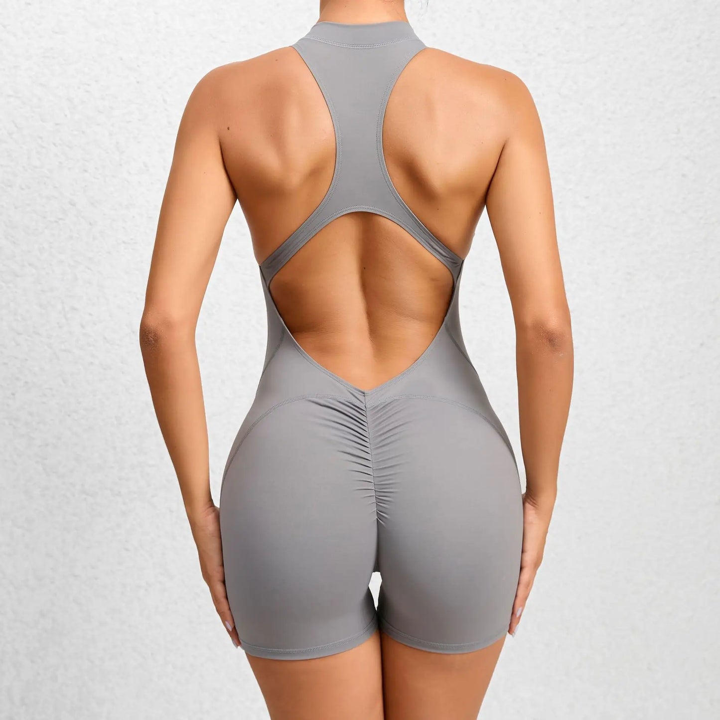 Back view of a woman wearing a gray sleeveless workout romper with open back and ruched detail