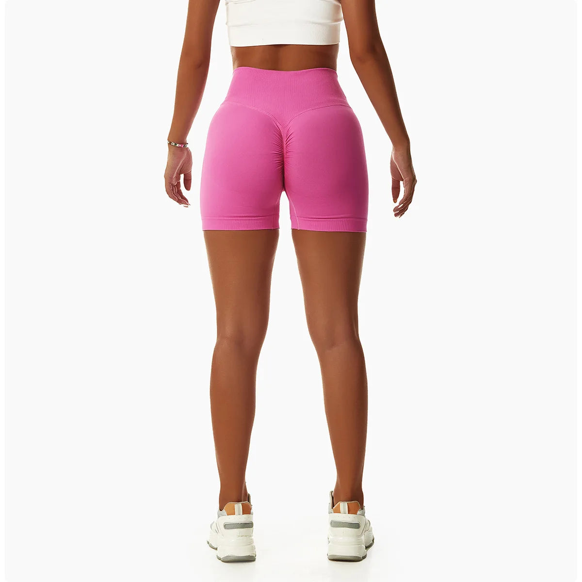 Back view of woman wearing pink high waist seamless yoga shorts with white crop top and sneakers