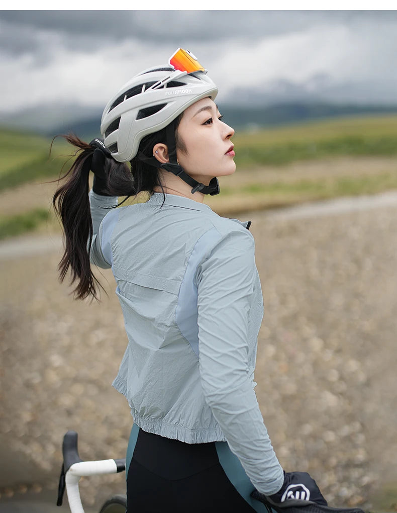 KiKis women's cycling windbreaker in light gray worn by cyclist with helmet on a gravel road