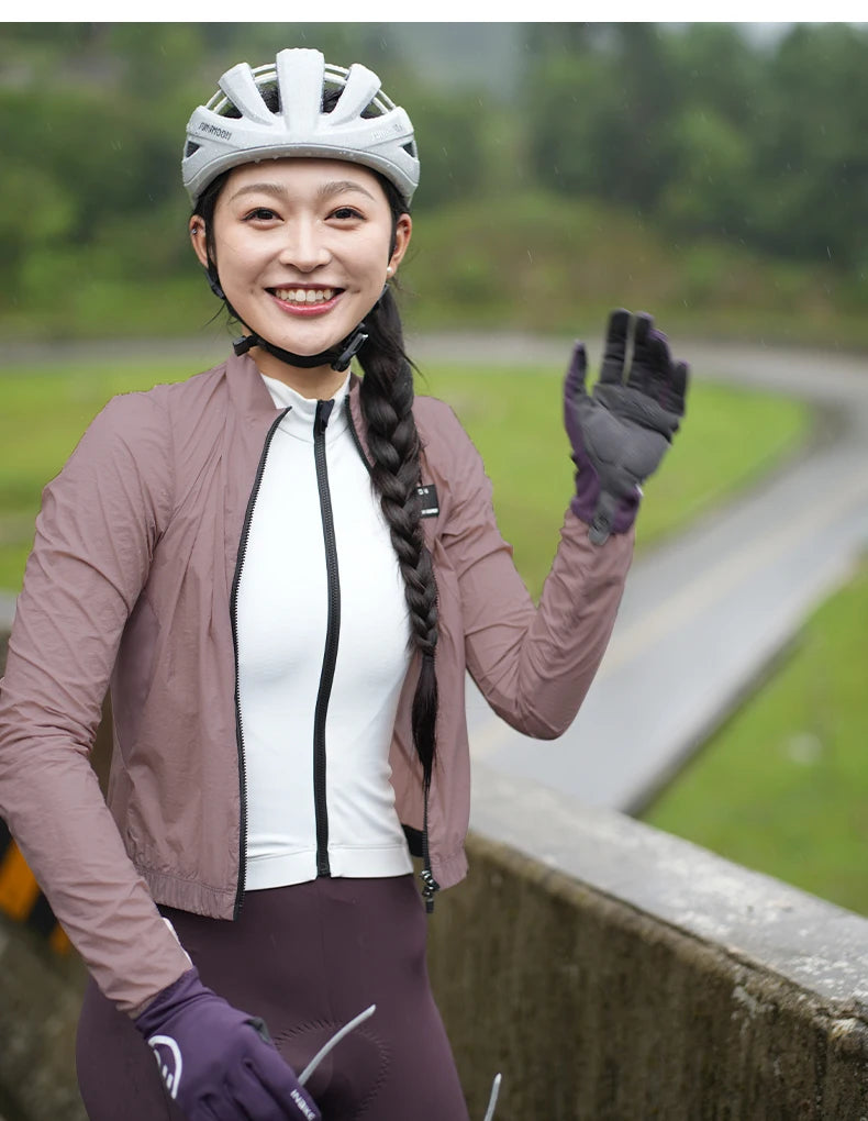 KiKis women's cycling windbreaker in light purple worn by smiling cyclist with helmet and gloves outdoors