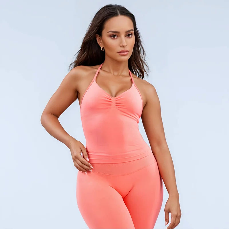 Woman wearing a coral open back yoga tank top for women with matching leggings posing against a light background