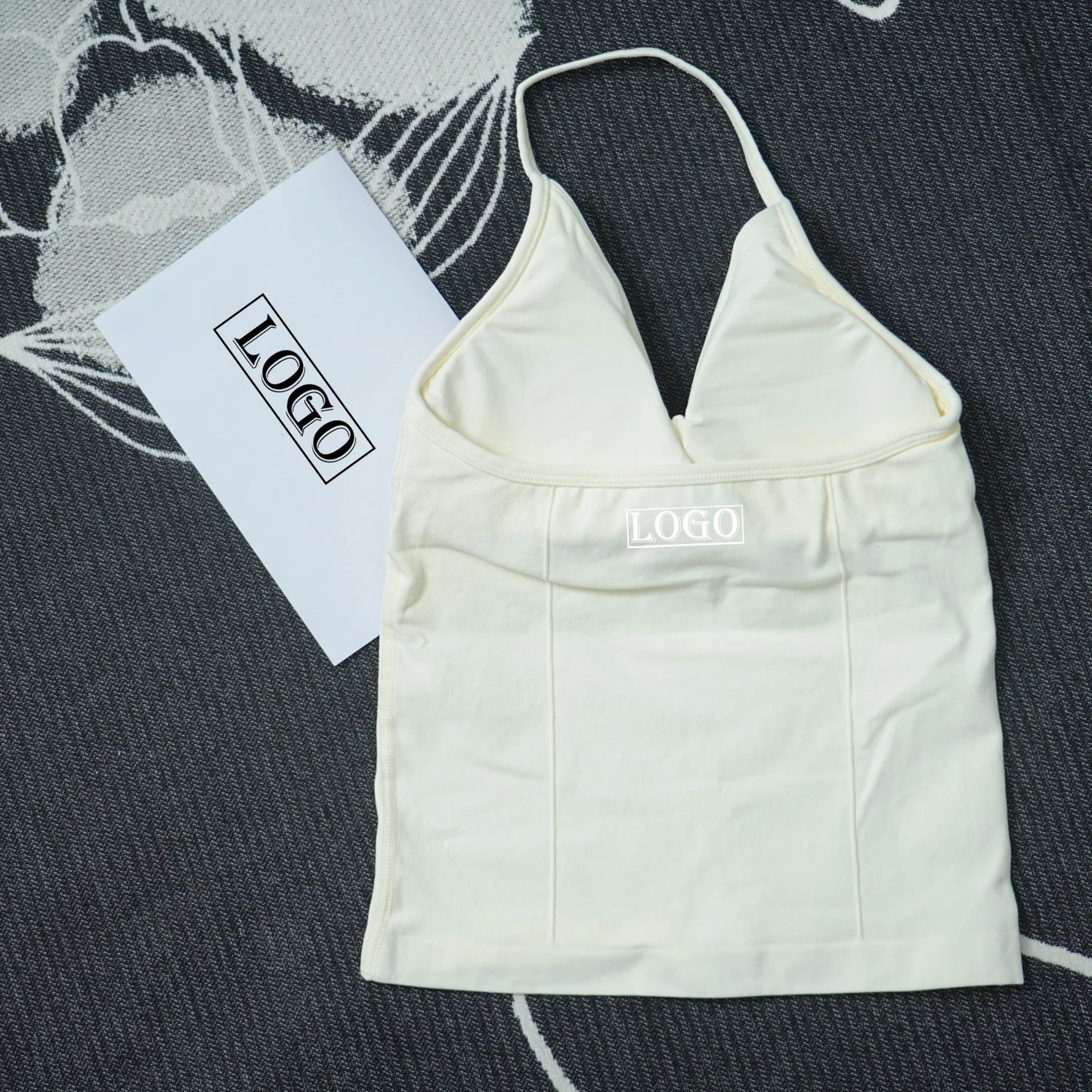 KiKis seamless yoga sports bra in white with thin straps and logo on front laid on dark textured fabric