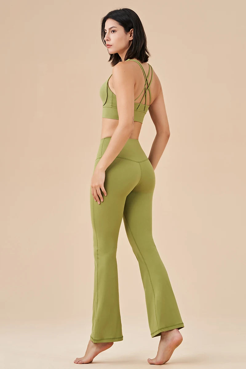 Woman wearing green womens bell bottom yoga pants with matching strappy sports bra standing barefoot