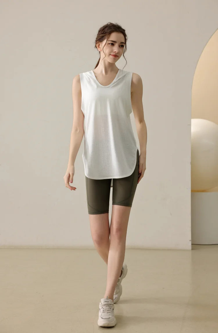 Woman wearing a white summer sleeveless workout hoodie with olive green bike shorts in a minimal indoor setting