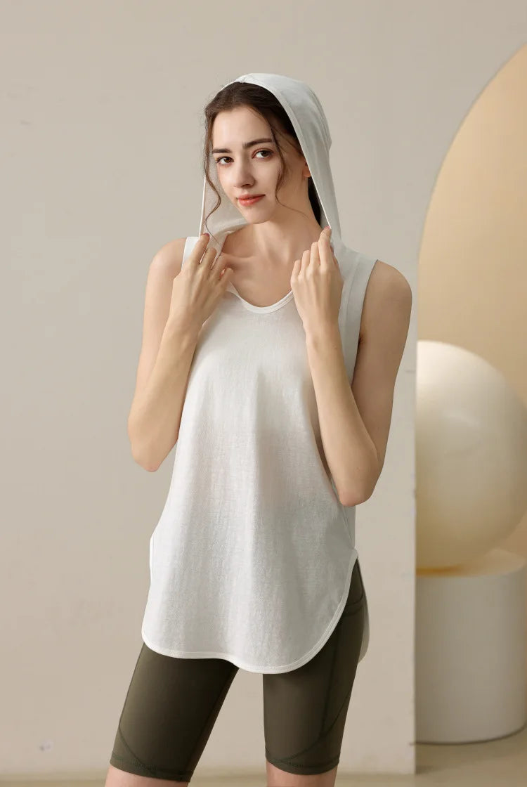 KiKis summer sleeveless workout hoodie in white worn by woman with hood up and hands near face
