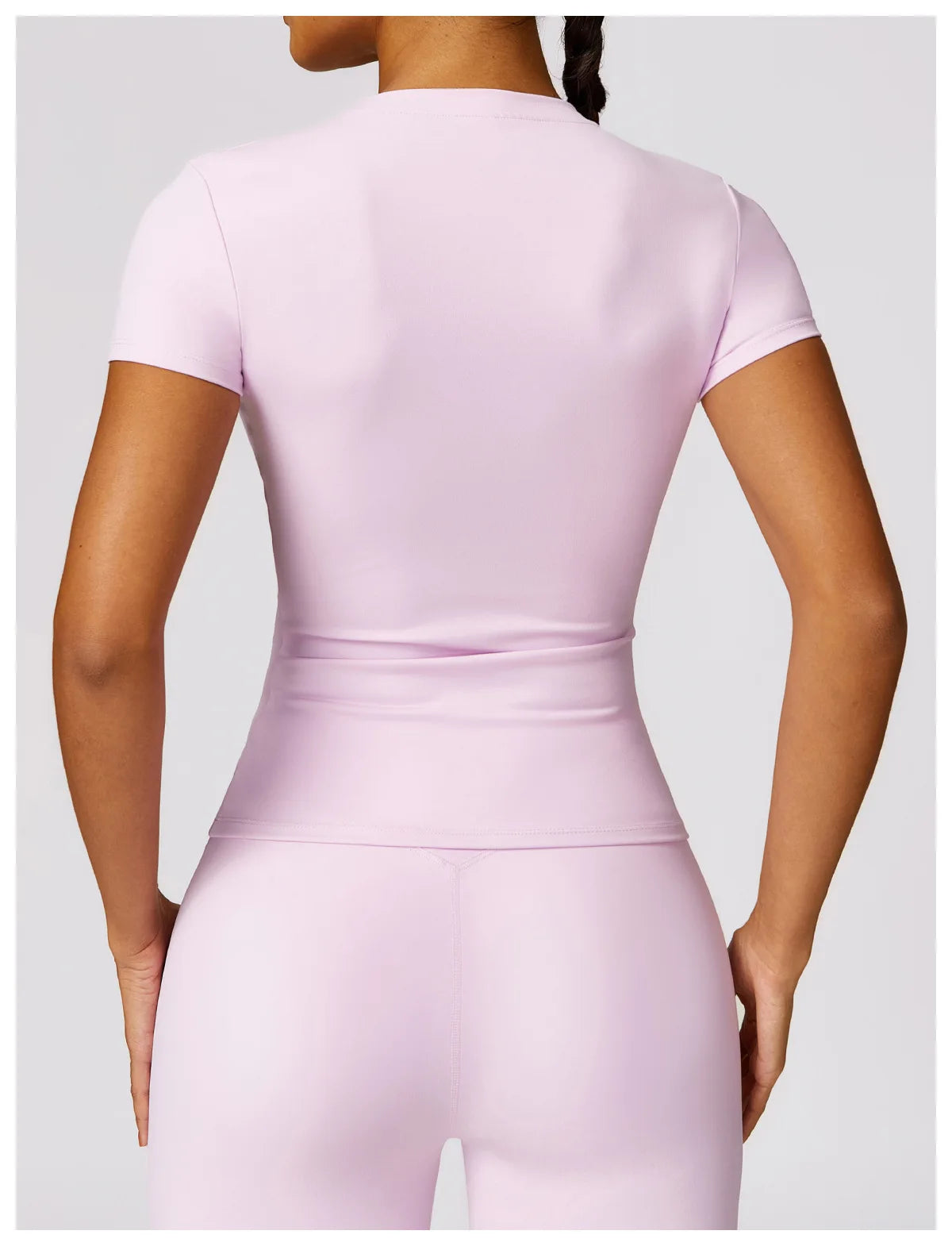 Back view of a woman wearing a light pink seamless yoga top for women with short sleeves and fitted design