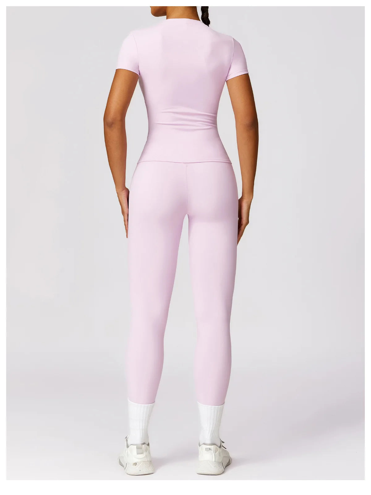Back view of woman wearing light pink seamless yoga top for women and matching leggings with white sneakers