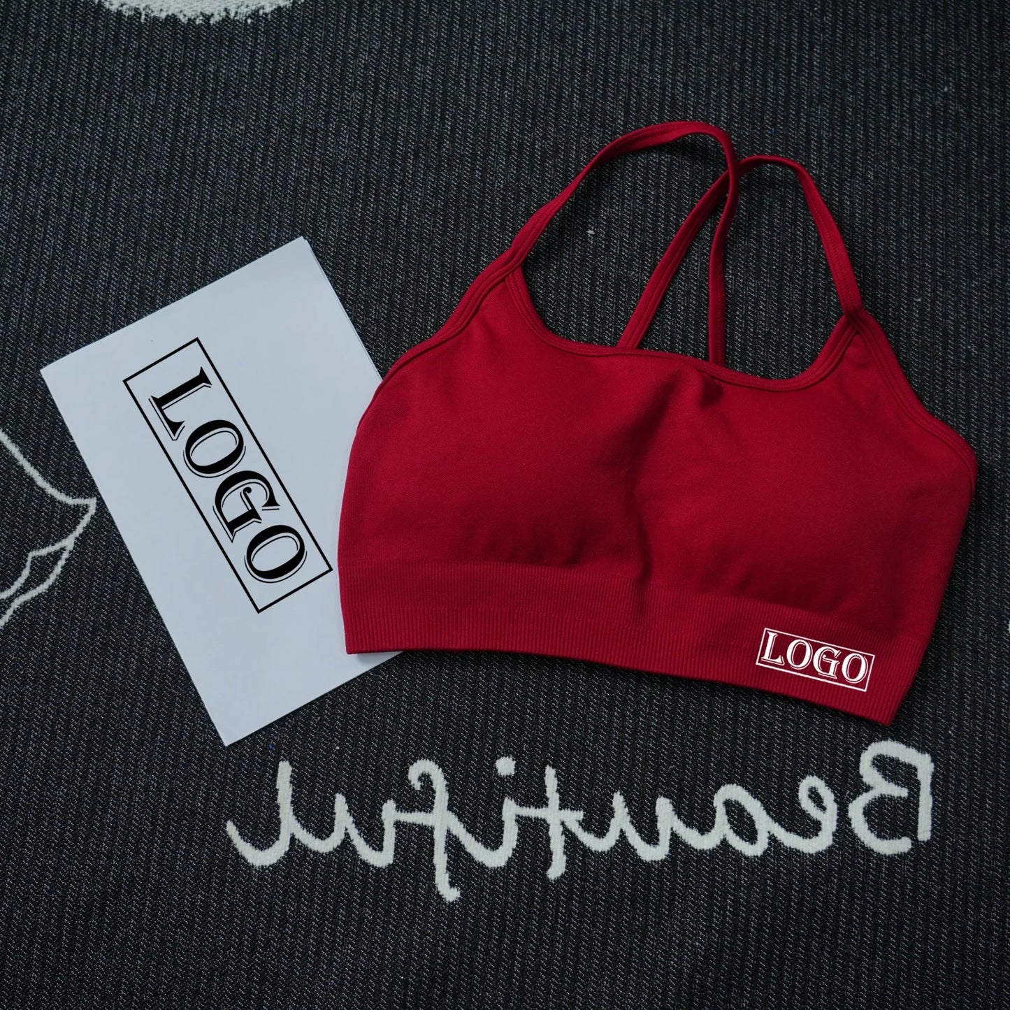KiKis women's seamless sports bra in red with thin straps laid on a black and white textured surface