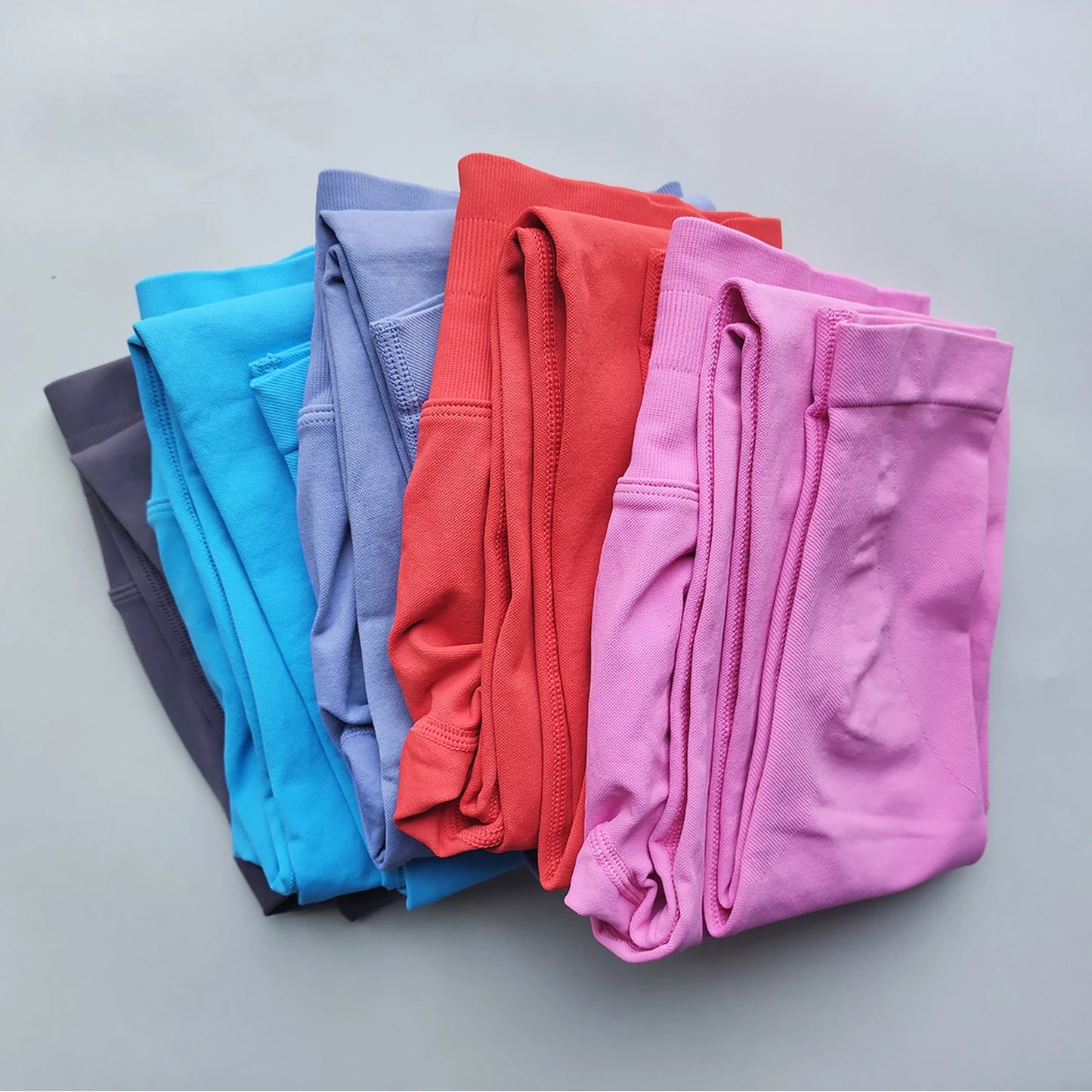 Stack of colorful Woman Scrunch Bum Flare Leggings folded neatly in pink, red, blue, purple, and black