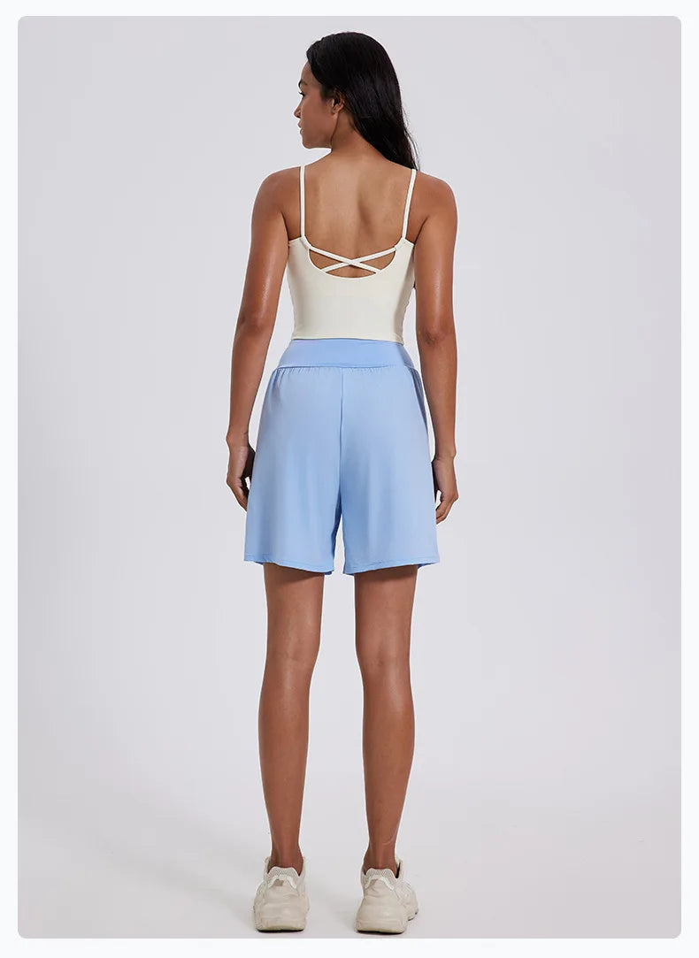 Back view of woman wearing light blue women's high waist running shorts with white tank top and sneakers