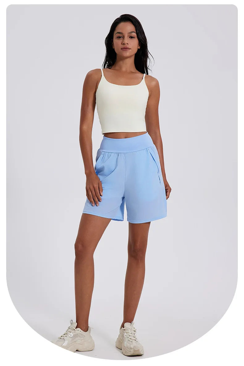 KiKis women's high waist running shorts in light blue worn with a white crop top and sneakers