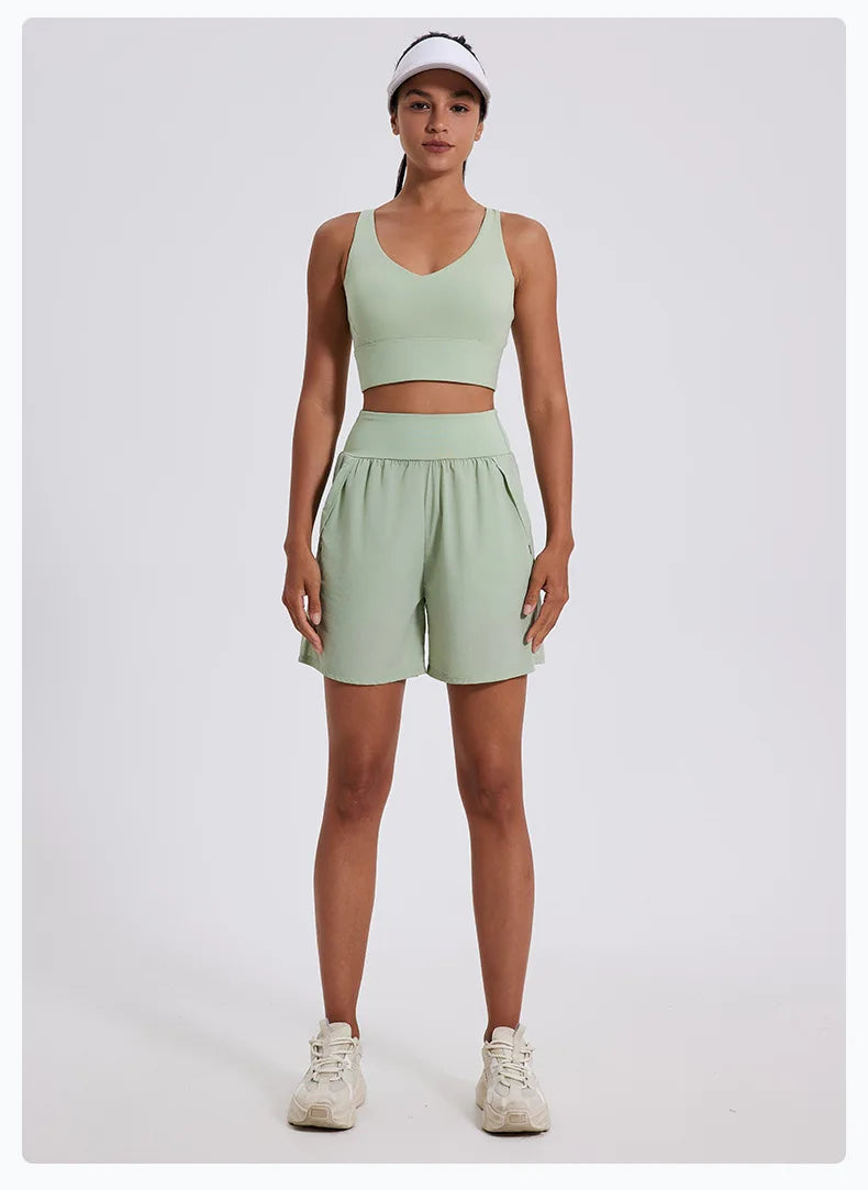 Woman wearing light green women's high waist running shorts and matching crop top with white visor and sneakers