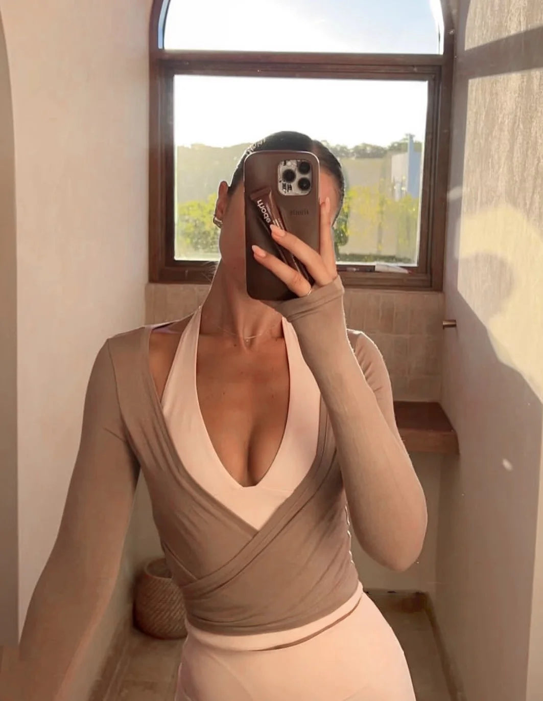 KiKis women's long sleeve yoga top in beige worn over a light sports bra during a mirror selfie