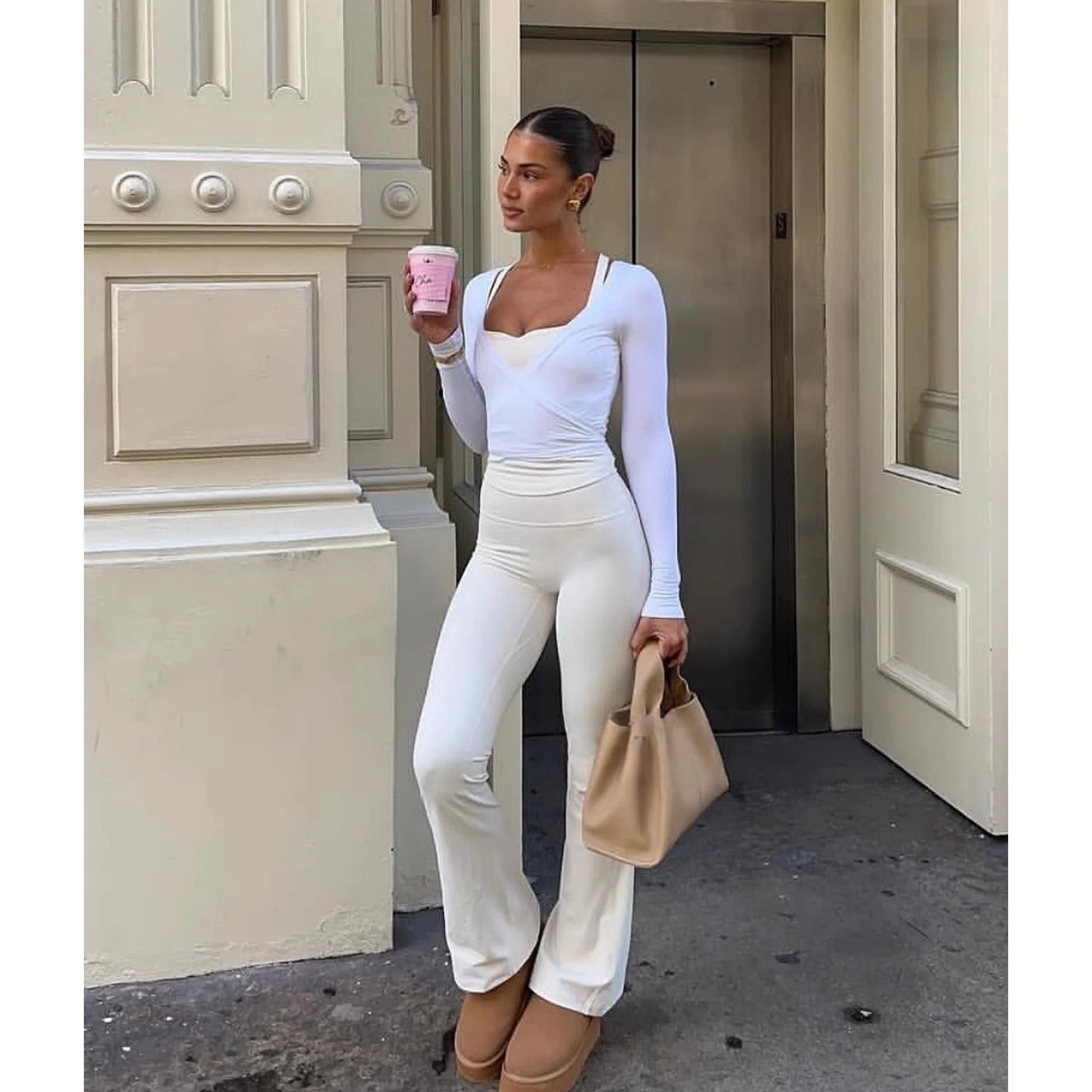Woman wearing white women's long sleeve yoga top and matching pants holding a beige handbag and pink cup