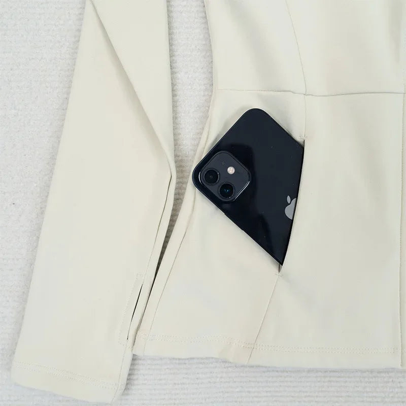 KiKis women's fleece yoga jacket in cream color with side pocket holding a black smartphone