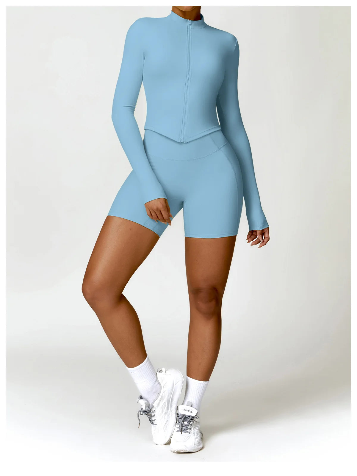 Light blue women's gym workout zip up top paired with matching fitted shorts and white sneakers