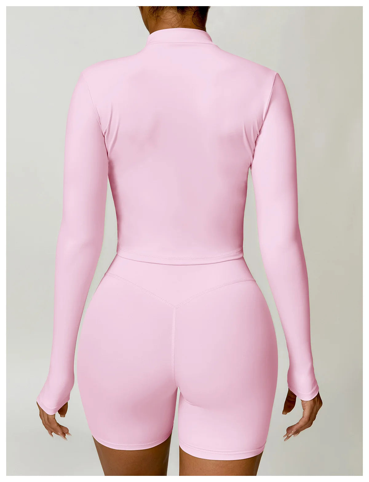 Back view of a woman wearing a pink women's gym workout zip up top with matching shorts