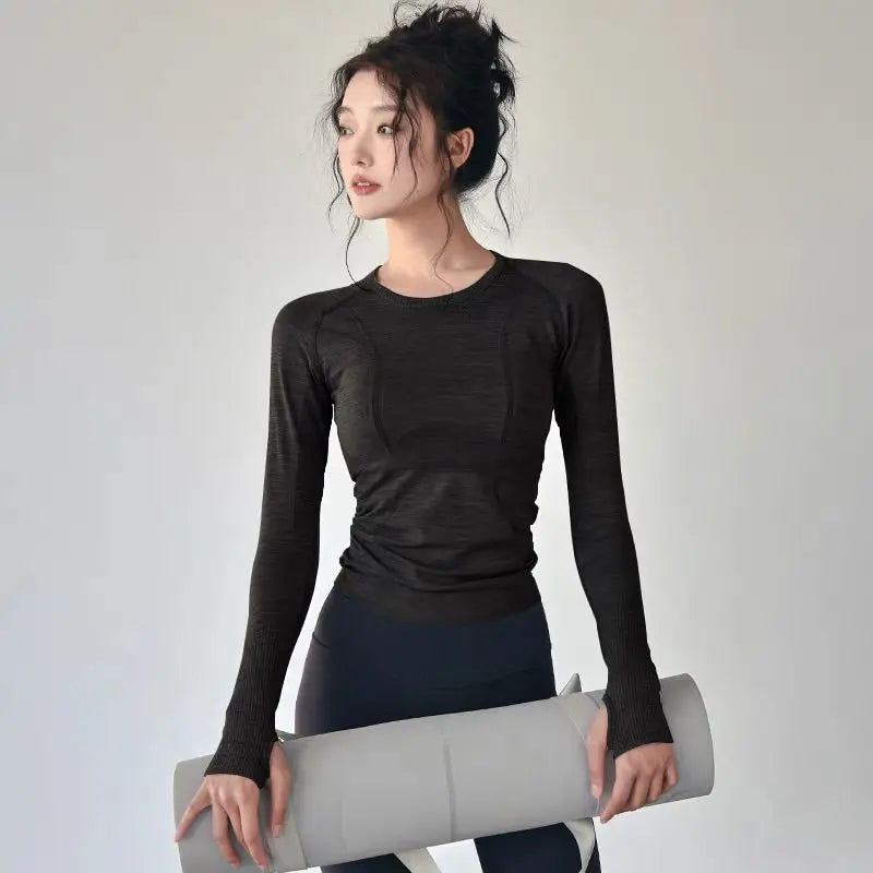 KiKis black women's long sleeve yoga top worn by woman holding a yoga mat indoors