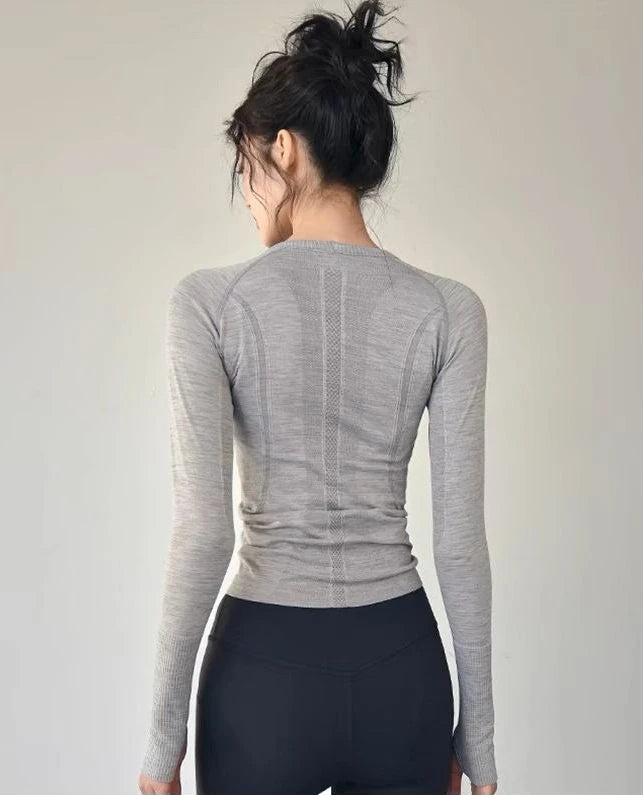Back view of a woman wearing a gray women's long sleeve yoga top paired with black leggings