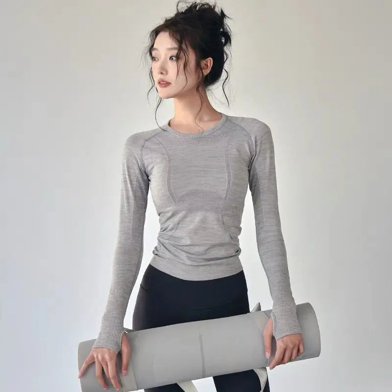 Woman wearing gray women's long sleeve yoga top holding a yoga mat in a fitness pose