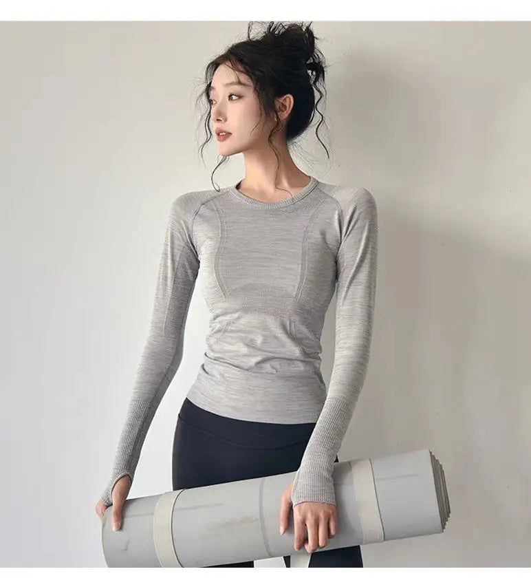 KiKis women's long sleeve yoga top in light gray worn by model holding a yoga mat