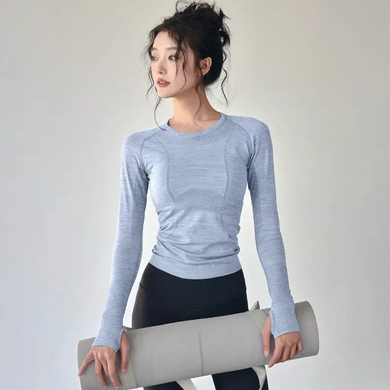KiKis women's long sleeve yoga top in light blue worn by model holding yoga mat