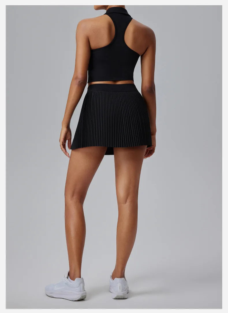Back view of model wearing KiKis Women's Organ Pleated Tennis Skirt in black with white sneakers